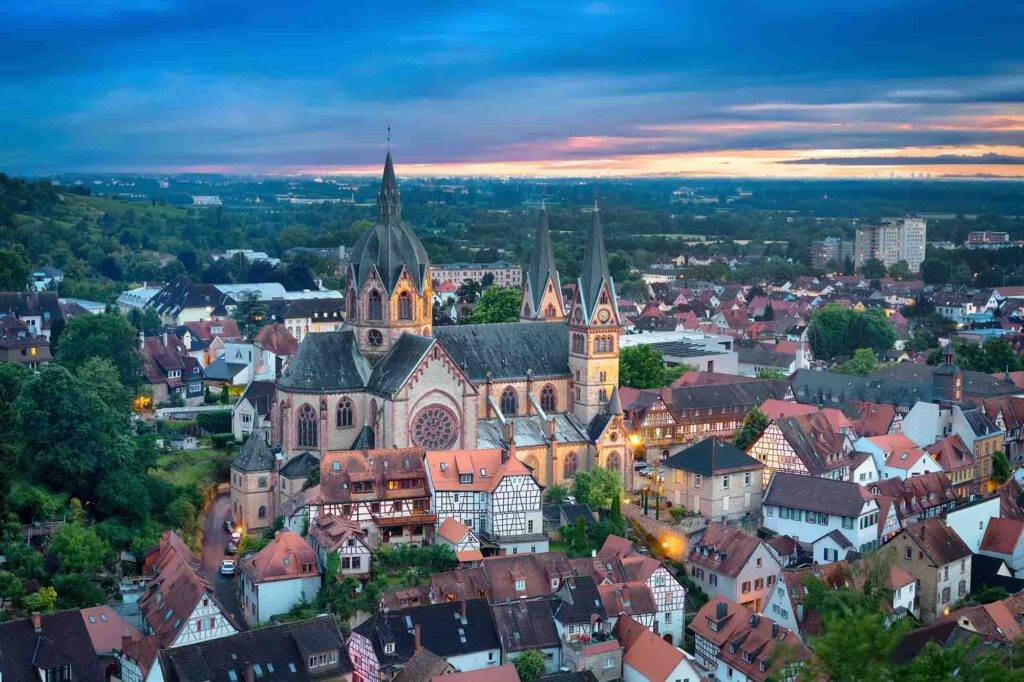 Luftaufnahme einer malerischen Stadt in der Abenddämmerung mit einer markanten Kirche mit zwei Glockentürmen und einer großen Fensterrose.